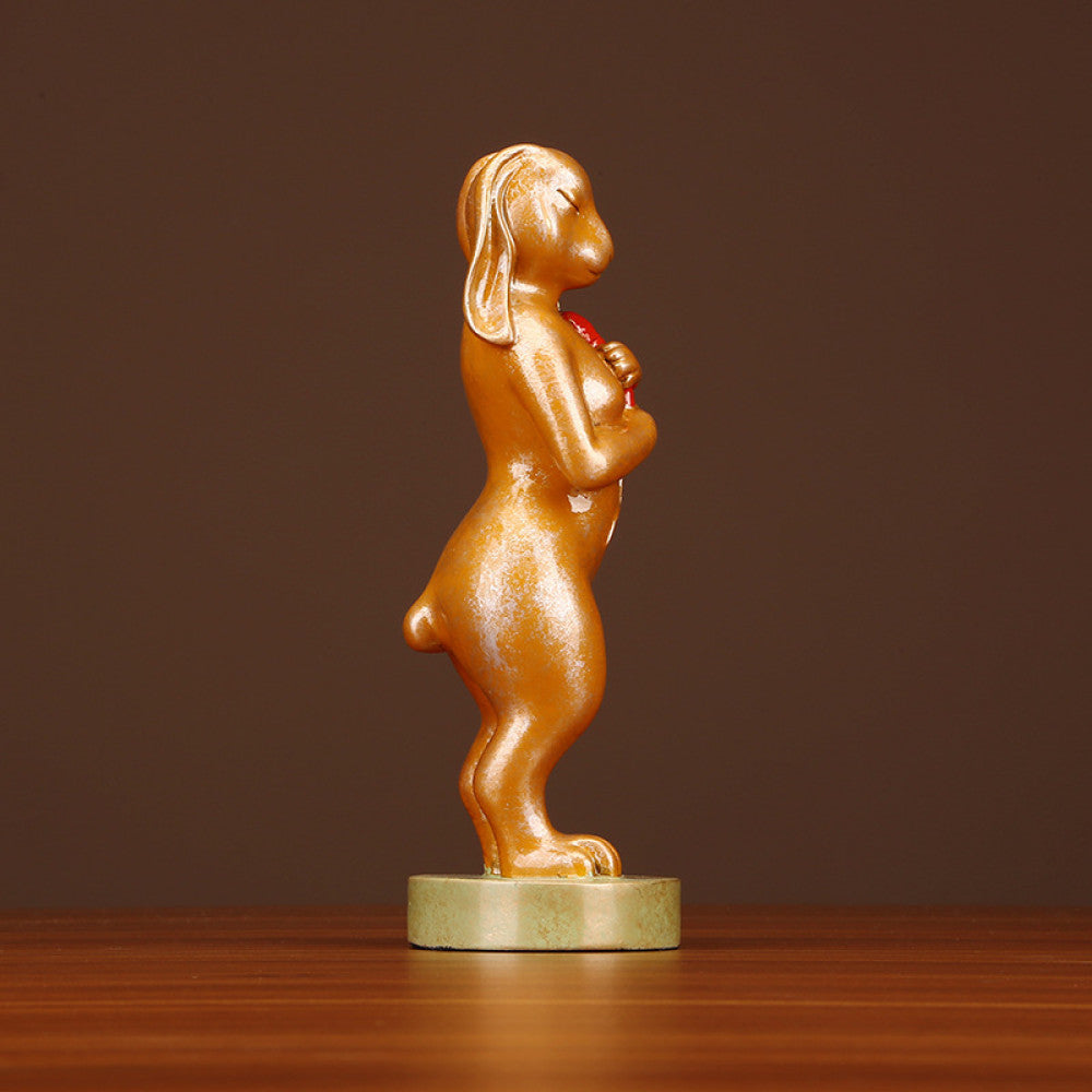 Golden rabbit statue in a standing pose holding a red accent, a symbol of good luck for home decor, placed on a greenish base against a brown background 01
