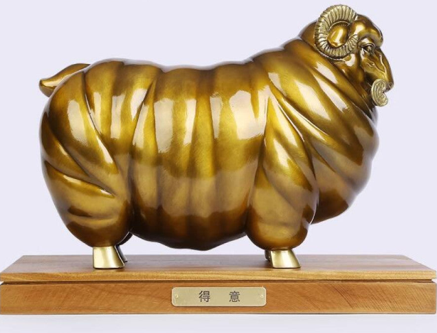 Golden ram statue with a wooden base, a Feng Shui symbol of wealth and success, displayed as elegant home decor against a light background