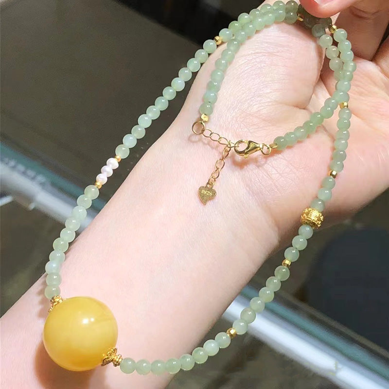 A beautiful necklace featuring light green jade beads, a large yellow amber focal bead, and elegant gold - toned accents,
