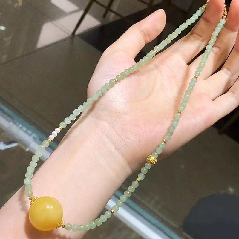 A beautiful necklace featuring light green jade beads, a large yellow amber focal bead, and elegant gold - toned accents, 01
