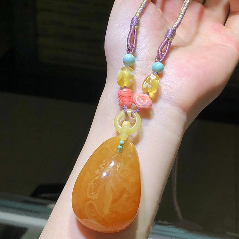 A stunning handmade necklace featuring a large, exquisite amber pendant paired with blue-green beads, white shell-shaped beads, and golden yellow decorative elements, all strung on a dark woven cord. 04