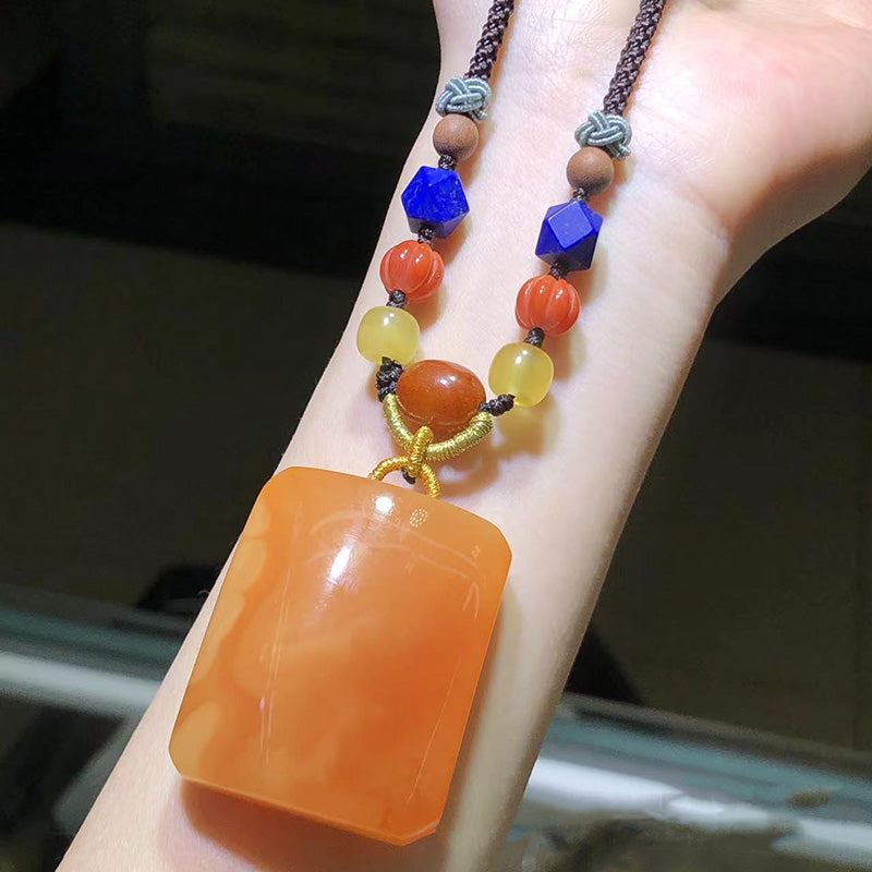 A stunning handmade necklace featuring a large, exquisite amber pendant paired with blue-green beads, white shell-shaped beads, and golden yellow decorative elements, all strung on a dark woven cord.01