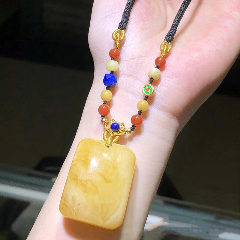 A stunning handmade necklace featuring a large, exquisite amber pendant paired with blue-green beads, white shell-shaped beads, and golden yellow decorative elements, all strung on a dark woven cord. 03