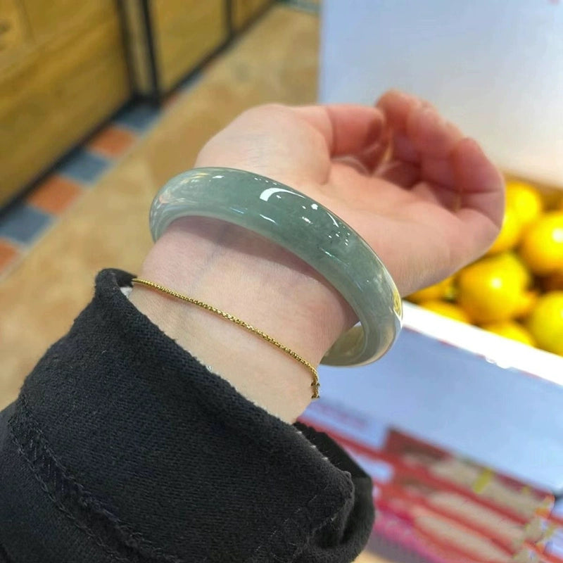 Hand wearing icy green jade bangle stacked with gold chain, natural jade jewelry in casual setting