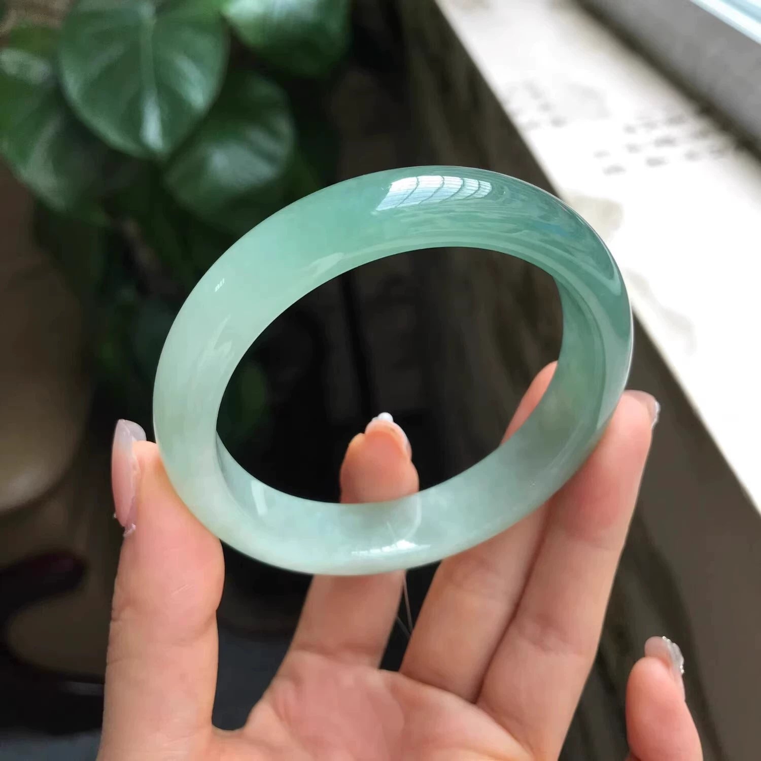 Hand holding icy light green natural jade bangle, translucent Chinese jade bracelet