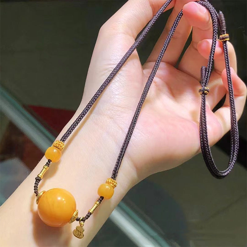A gorgeous necklace featuring a prominent large amber bead, complemented by smaller amber beads and gold - toned decorative elements, strung on a dark braided cord. Perfect accessory to elevate any look.