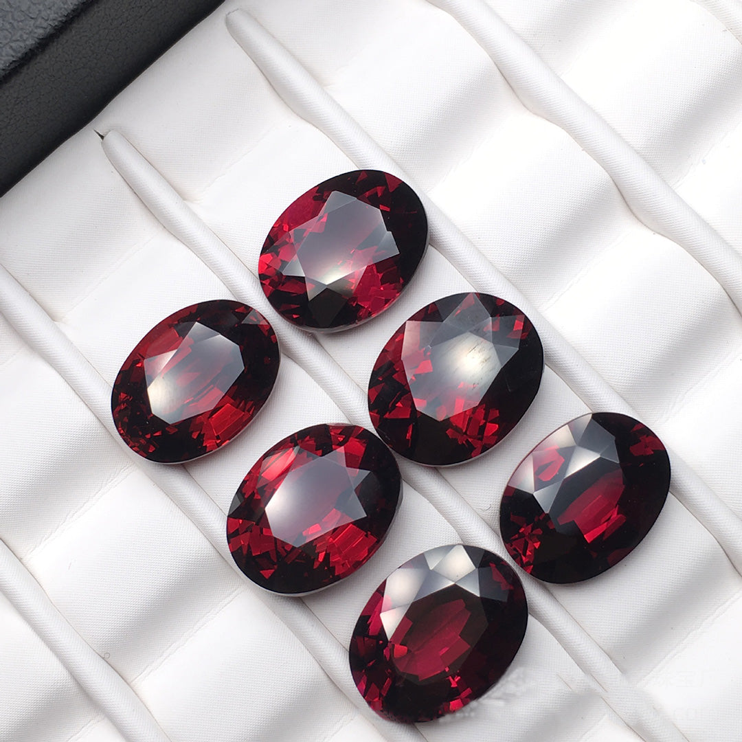 Six oval-cut ruby garnet rough stones, crystal clear, displayed on a white tray.