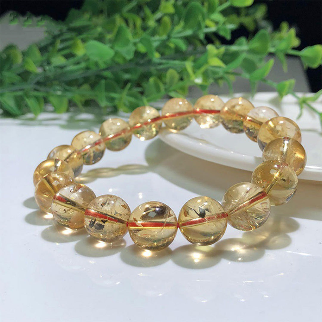 A natural citrine bead bracelet held in a hand, featuring transparent to translucent beads with a beautiful yellow - orange hue, strung together on an orange cord. 01