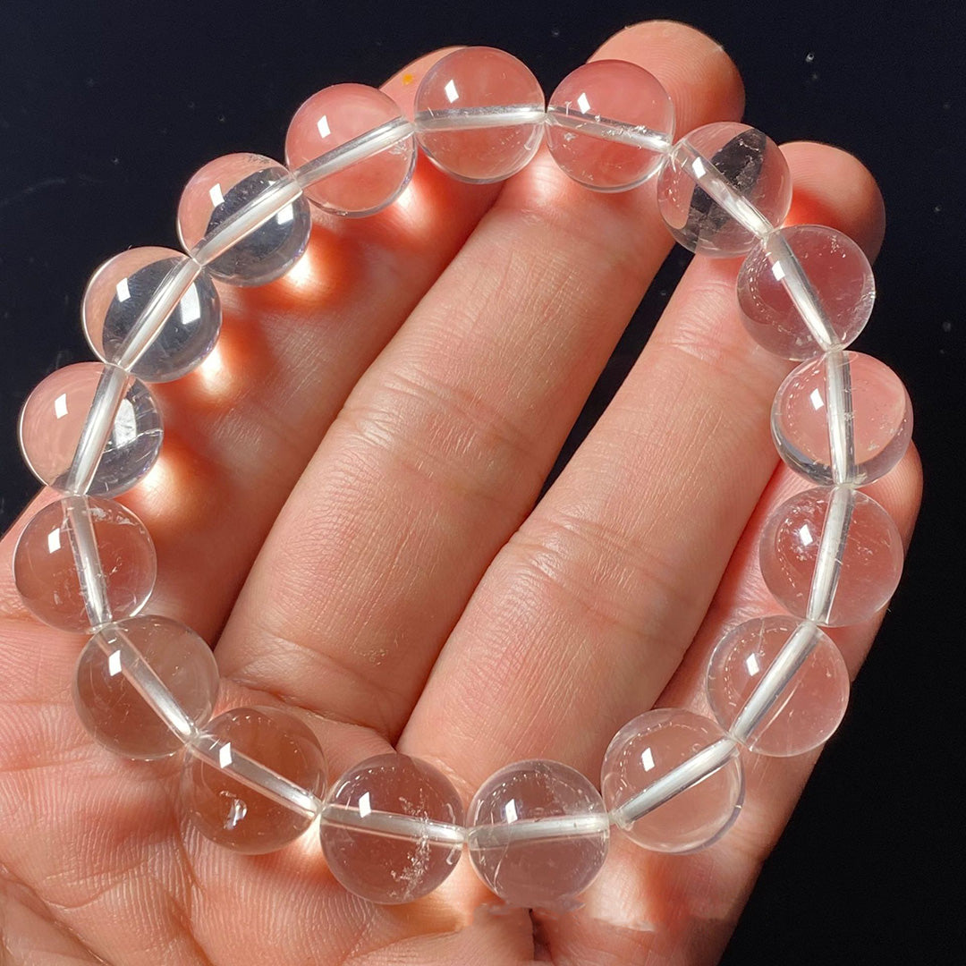 A natural clear quartz crystal bead bracelet held in a hand, showcasing transparent and glossy beads strung together.