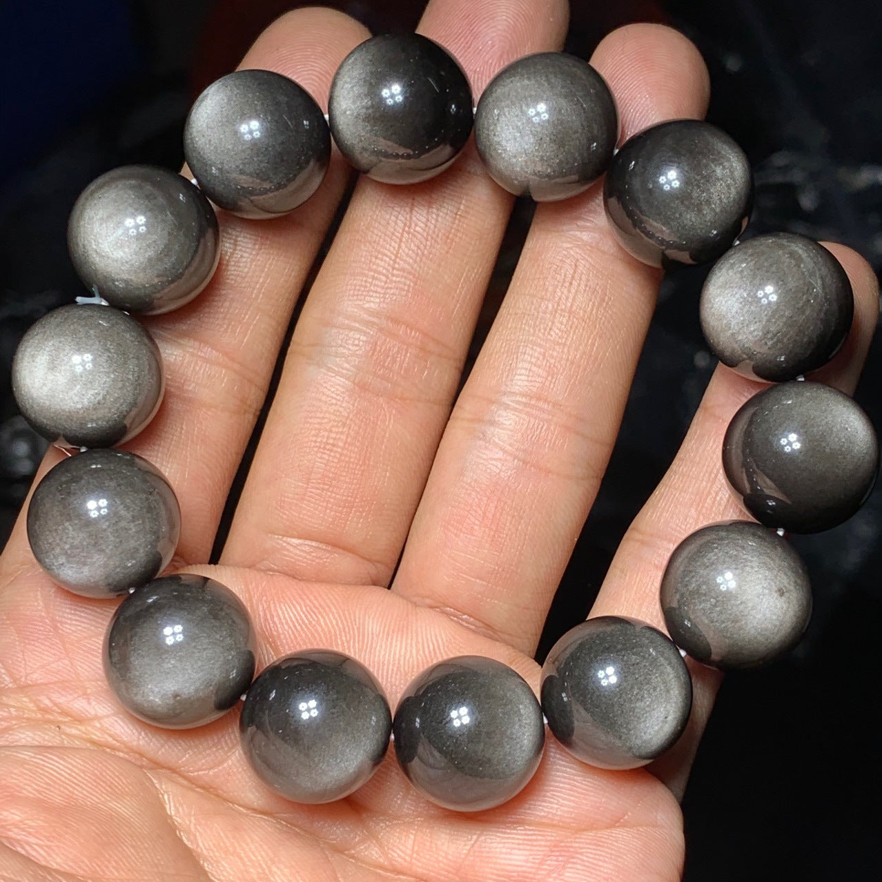 A hand - held natural gray moonstone bead bracelet, featuring smooth, round beads with a soft, shimmery luster.