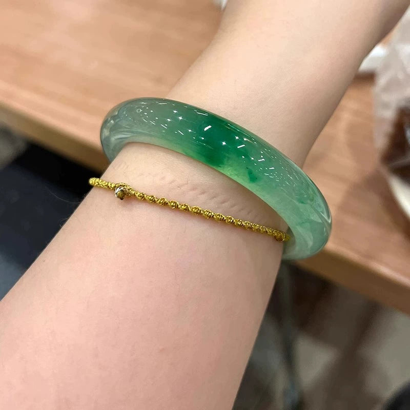 Wrist wearing natural green engraved jadeite bangle stacked with delicate gold bracelet in everyday style
