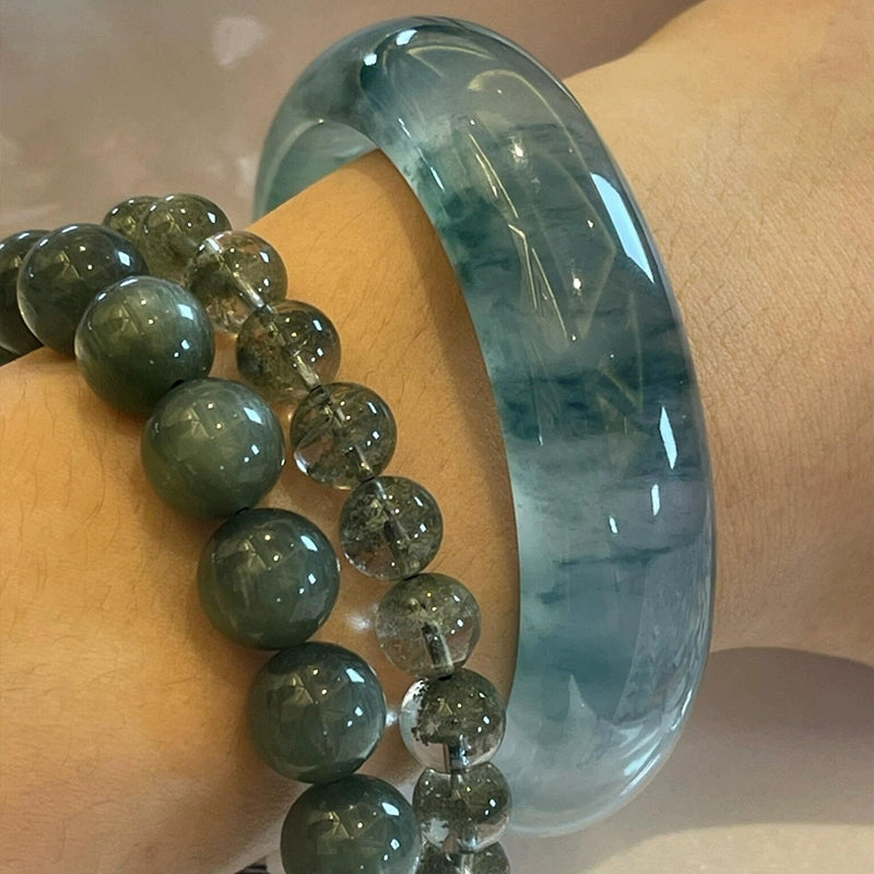Wrist wearing natural icy blue-green jadeite bangle stacked with dark green gemstone bead bracelets