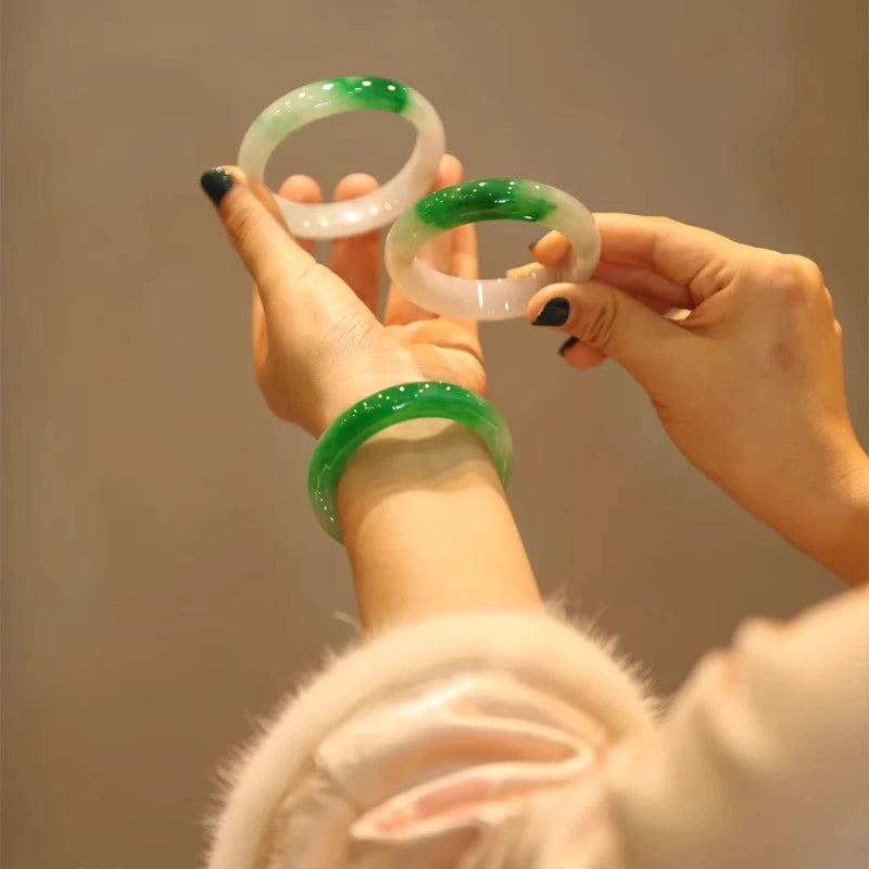 Hands holding multiple natural icy green gradient jadeite bangles with plant background 01