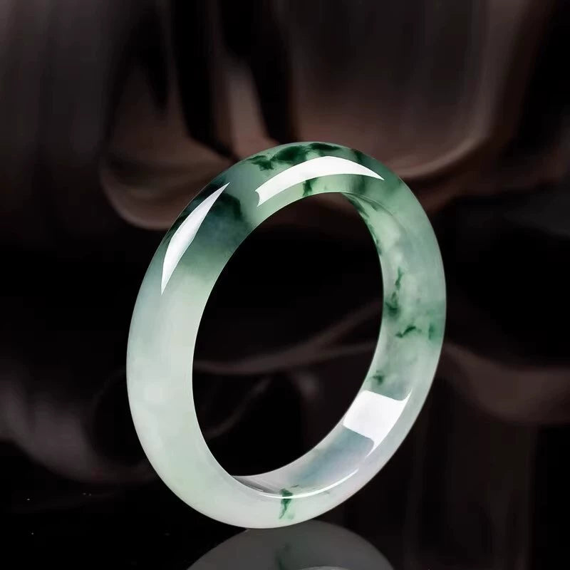 Natural icy jadeite bangle with emerald green veins on dark reflective background