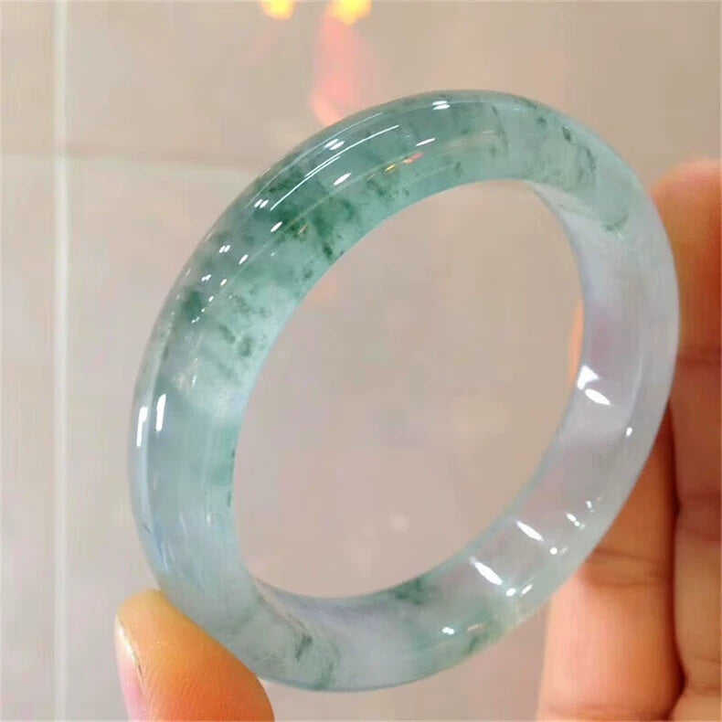 Hand holding natural icy jadeite bangle with green flecks against light background