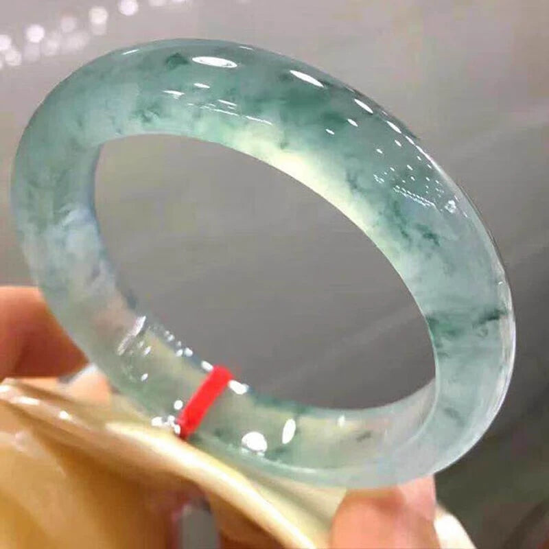 Hand holding natural icy jadeite bangle with green flecks against light background