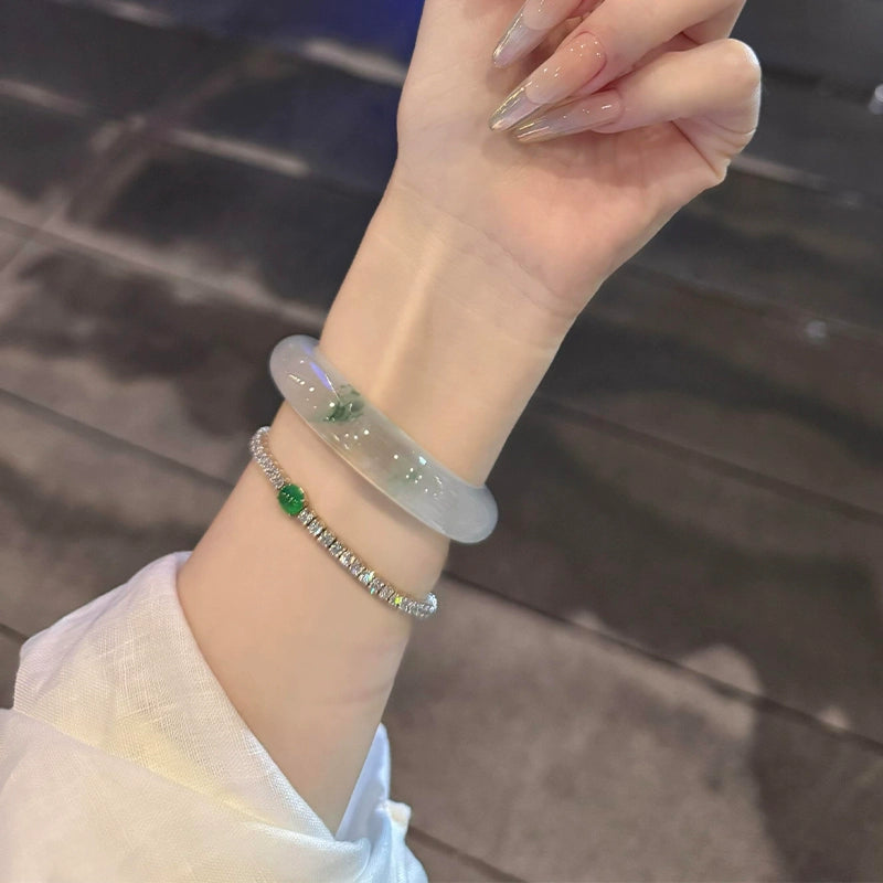 Wrist wearing natural icy jadeite bangle with green flecks stacked with diamond and gemstone bracelet in elegant style