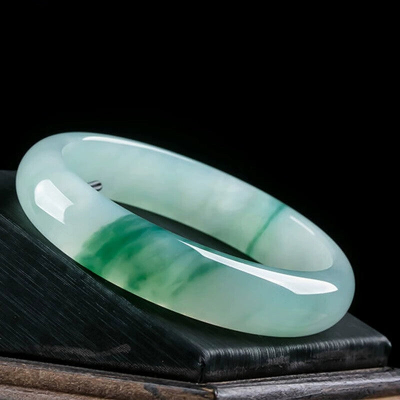 Natural icy jadeite bangle with green patches placed on dark wooden display stand against black background