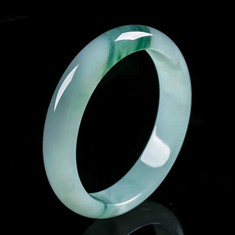 Natural icy jadeite bangle with green patches placed on dark wooden display stand against black background 01