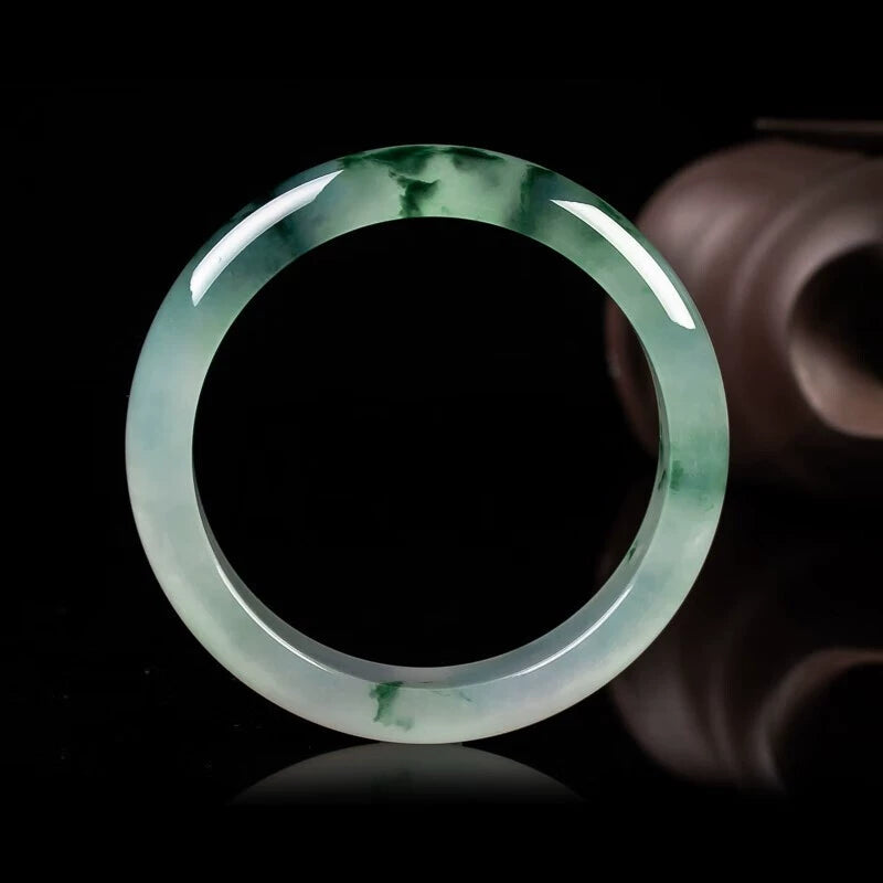 Natural icy jadeite bangle with green patches displayed against black background with ceramic accents