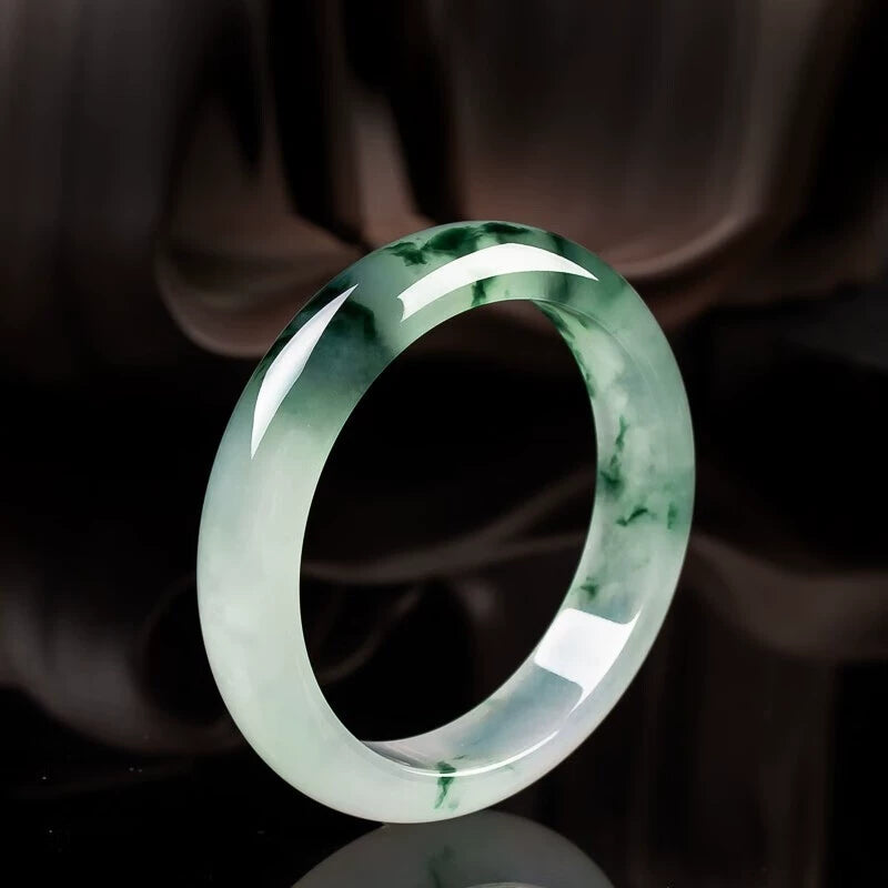 Natural icy jadeite bangle with green patches displayed against black background with ceramic accents 01