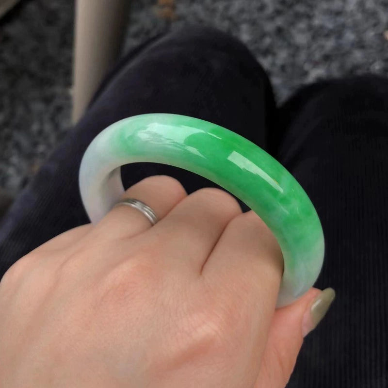 Hand holding natural icy jadeite bangle with spring green gradient