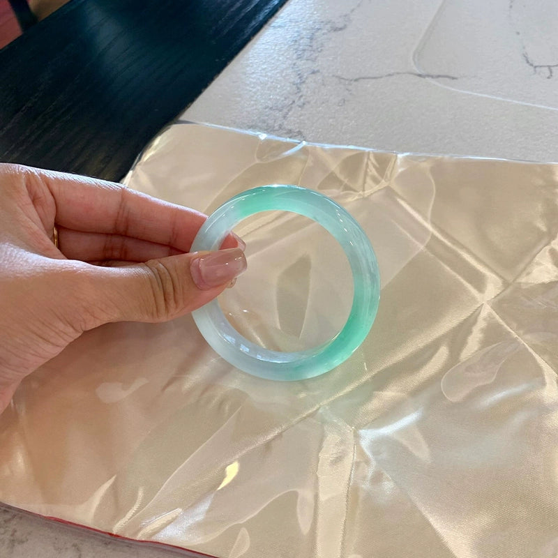 Natural icy jadeite bangle with vivid green accents placed on silky fabric 01