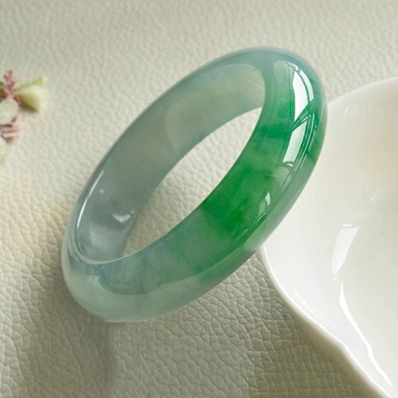 Natural icy jadeite bangle with vivid green patches placed near white dish