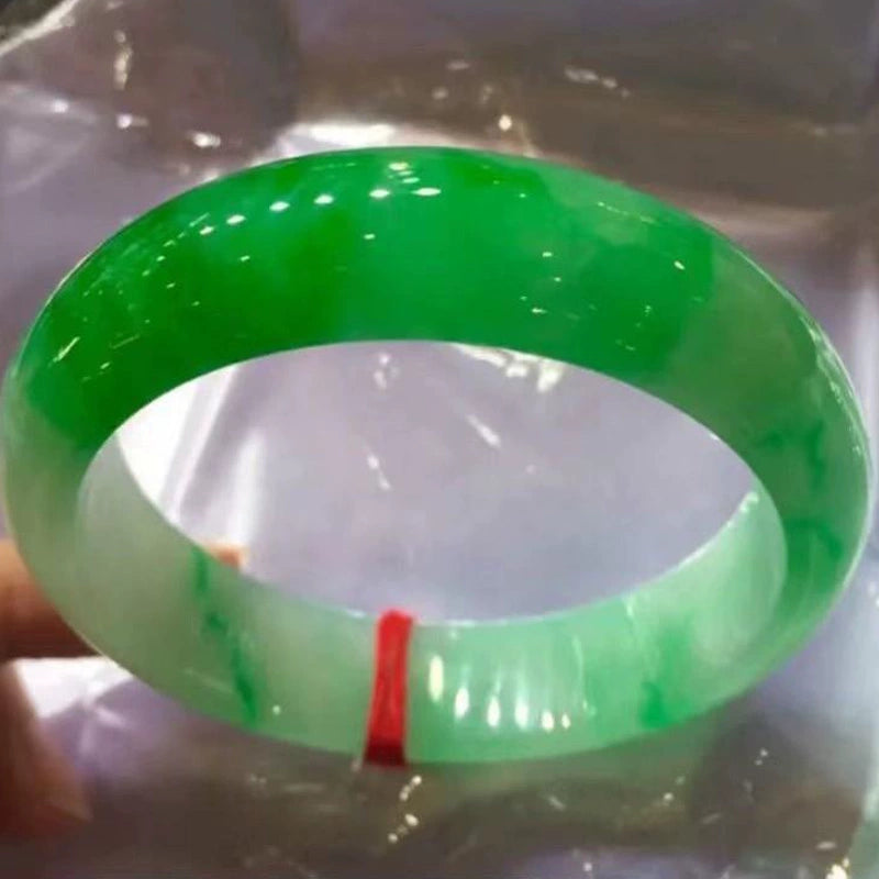Hand holding natural icy jadeite bangle with vivid green patches and red string on plastic background