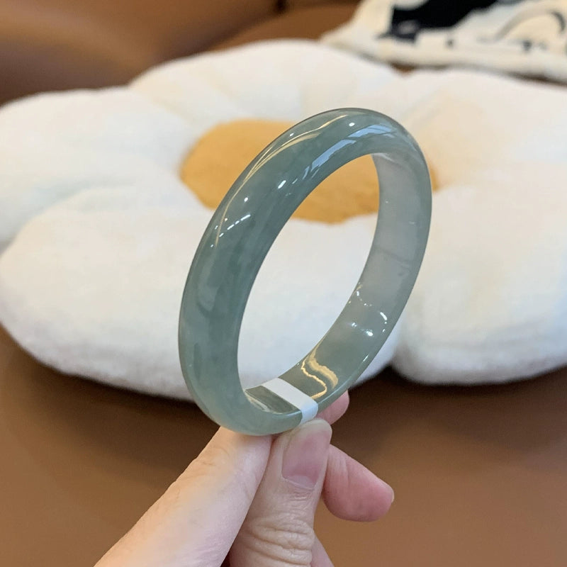 Hand holding natural icy light grayish green jadeite bangle with plush flower background