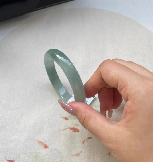 Hand holding natural icy light green jade bangle with Chinese goldfish pattern background