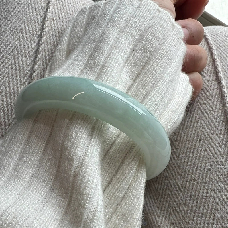 Hands holding two natural icy light green jade bangles by jewelry case 01