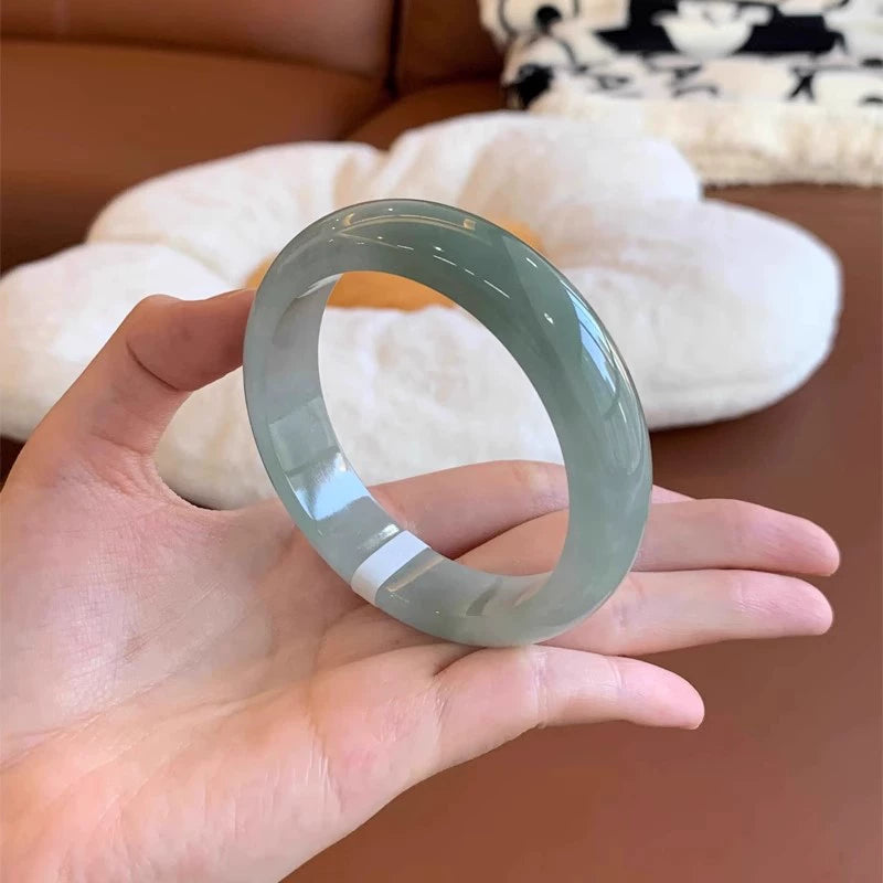 Hand holding natural icy light green jadeite bangle