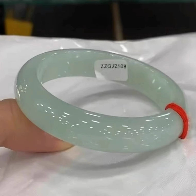 Hand holding natural icy light green jadeite bangle with red string