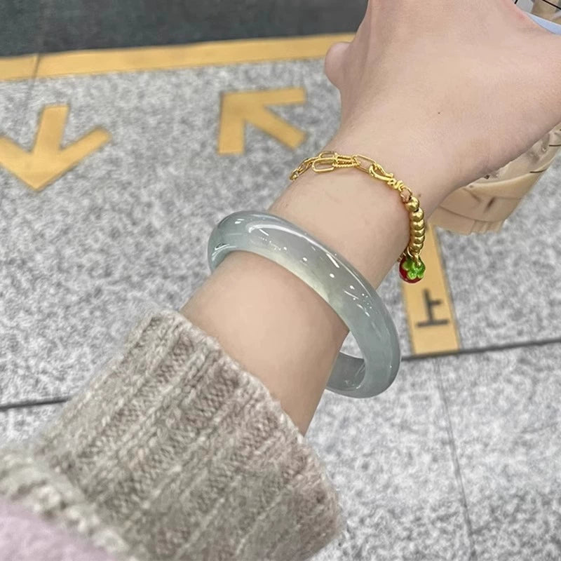 Wrist wearing natural icy light green jadeite bangle and gold bracelet in urban setting