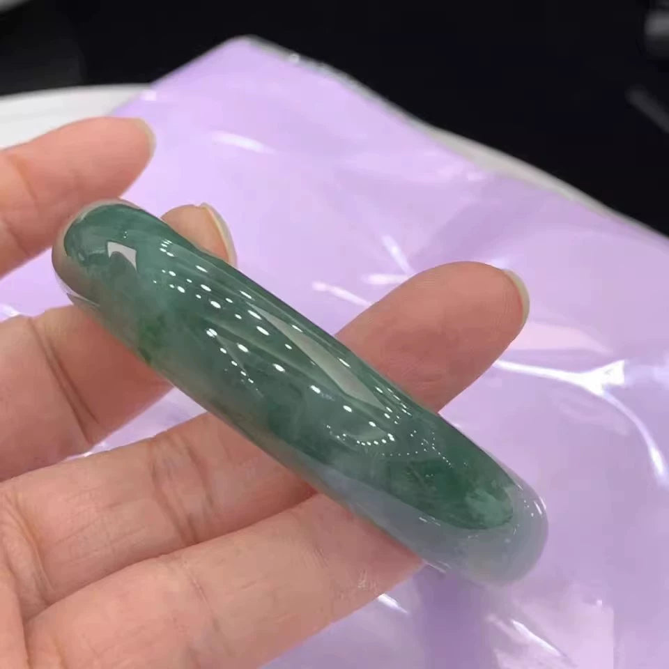 Hand holding natural icy moss-infused green jadeite bangle