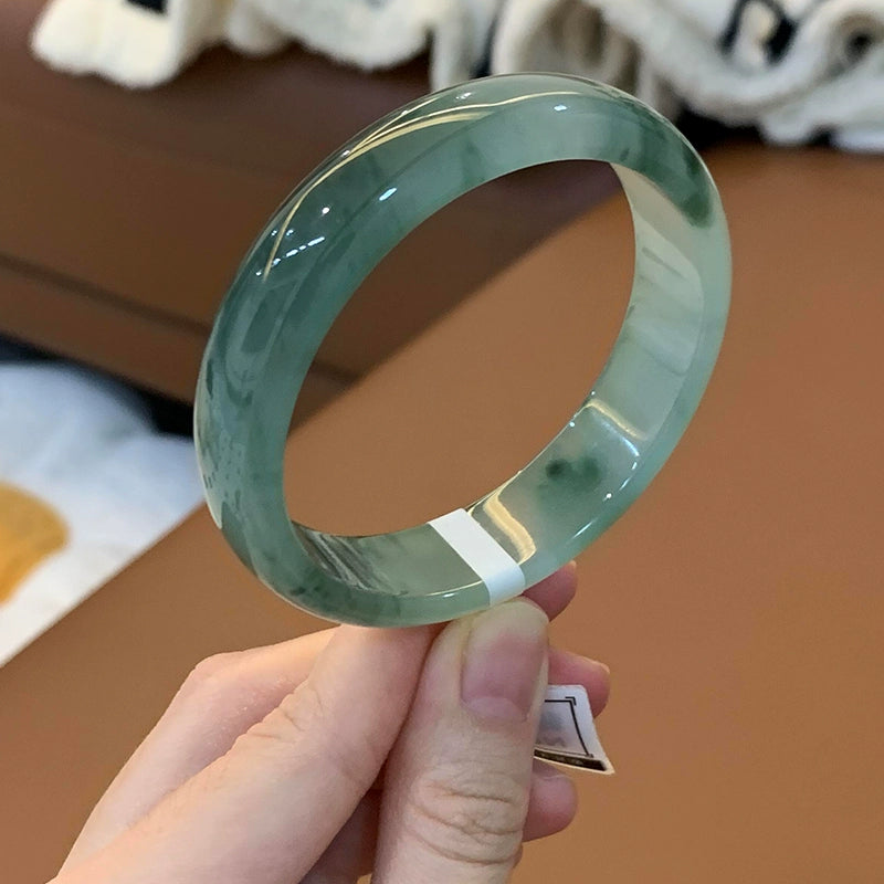 Hand holding natural icy moss-infused light green jade bangle