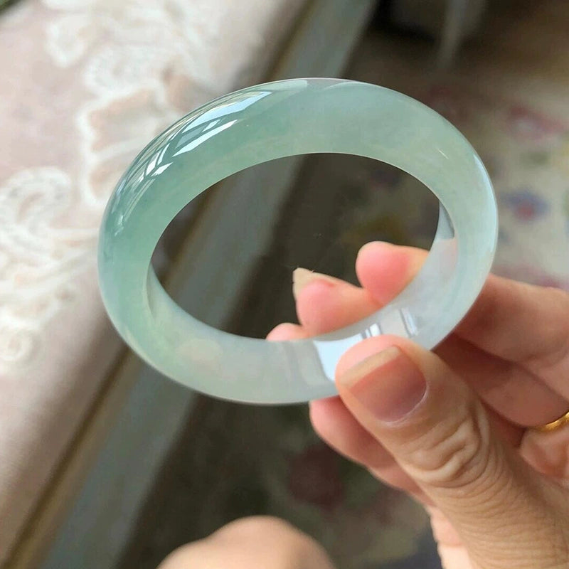 Hand holding natural icy translucent light green jadeite bangle