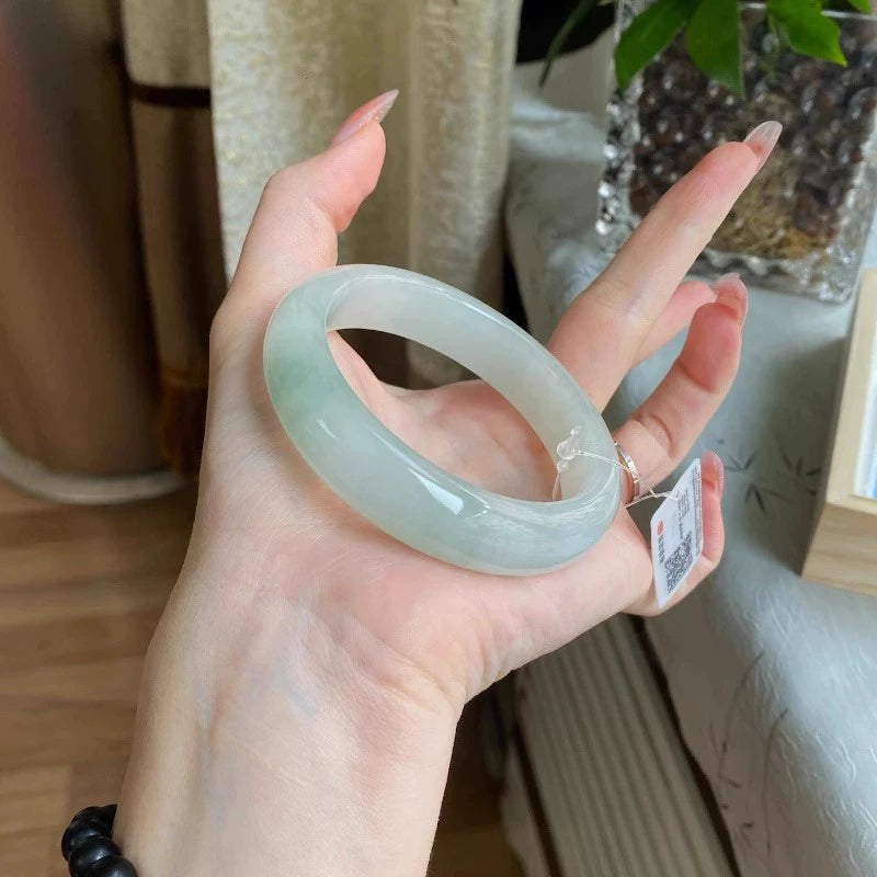Hand holding natural icy translucent light green jadeite bangle with tag