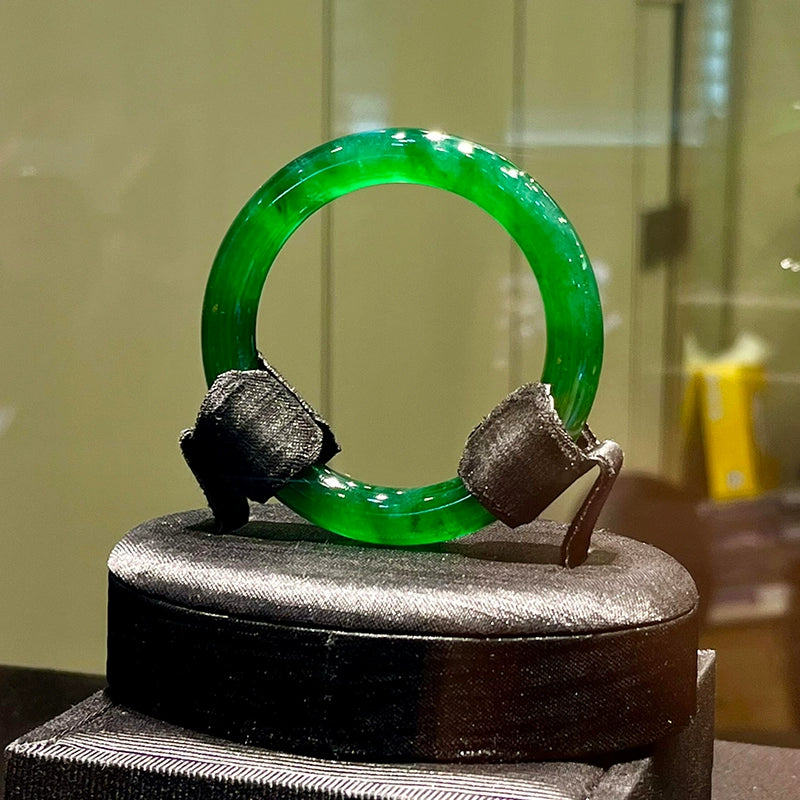 Natural imperial green icy jadeite bangle displayed on black jewelry stand in showcase