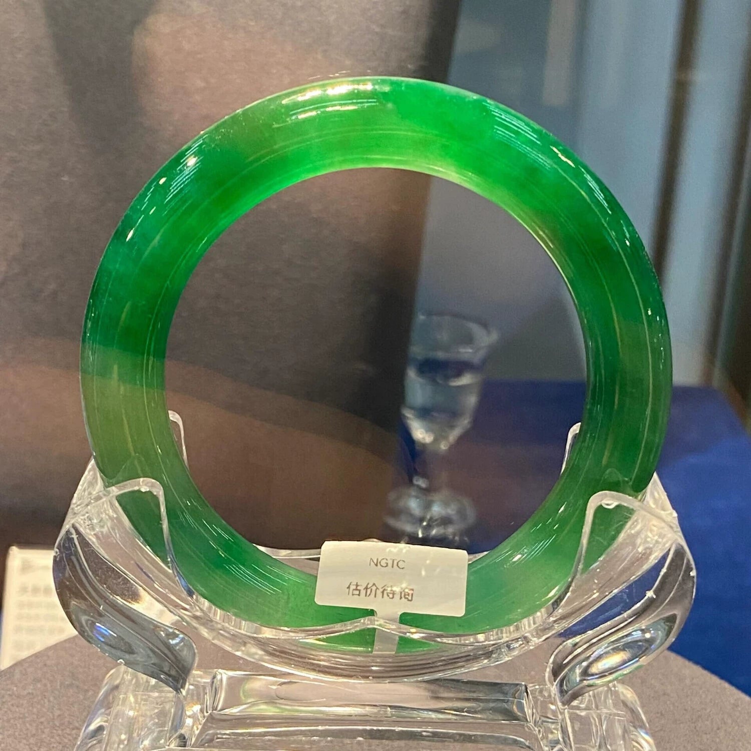Natural imperial green icy jadeite bangle on clear display stand with price tag in jewelry exhibition
