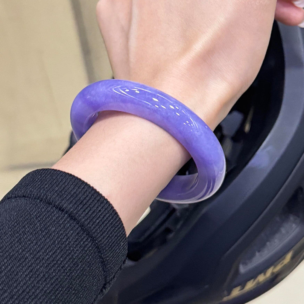 Hand wearing natural lavender jadeite bangle against dark-toned background