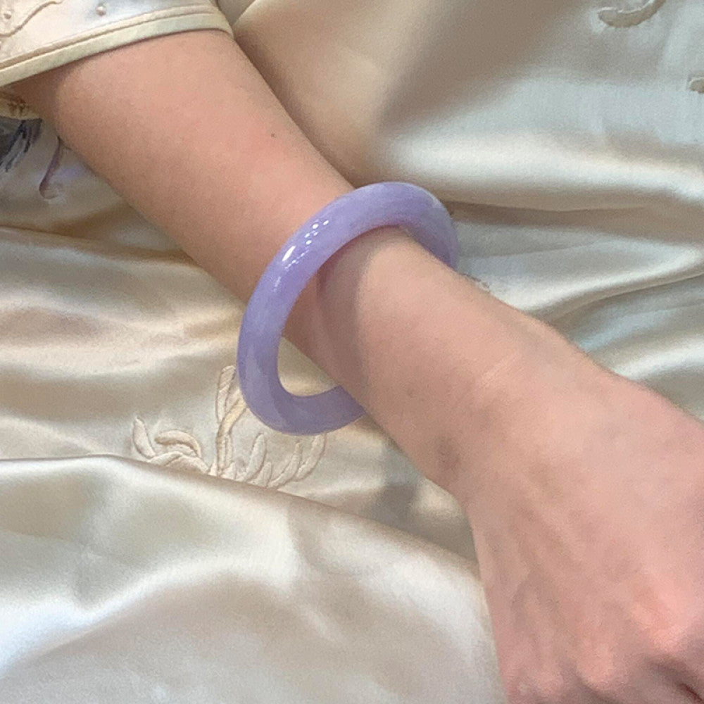 Wrist wearing natural lavender jadeite bangle on embroidered satin fabric