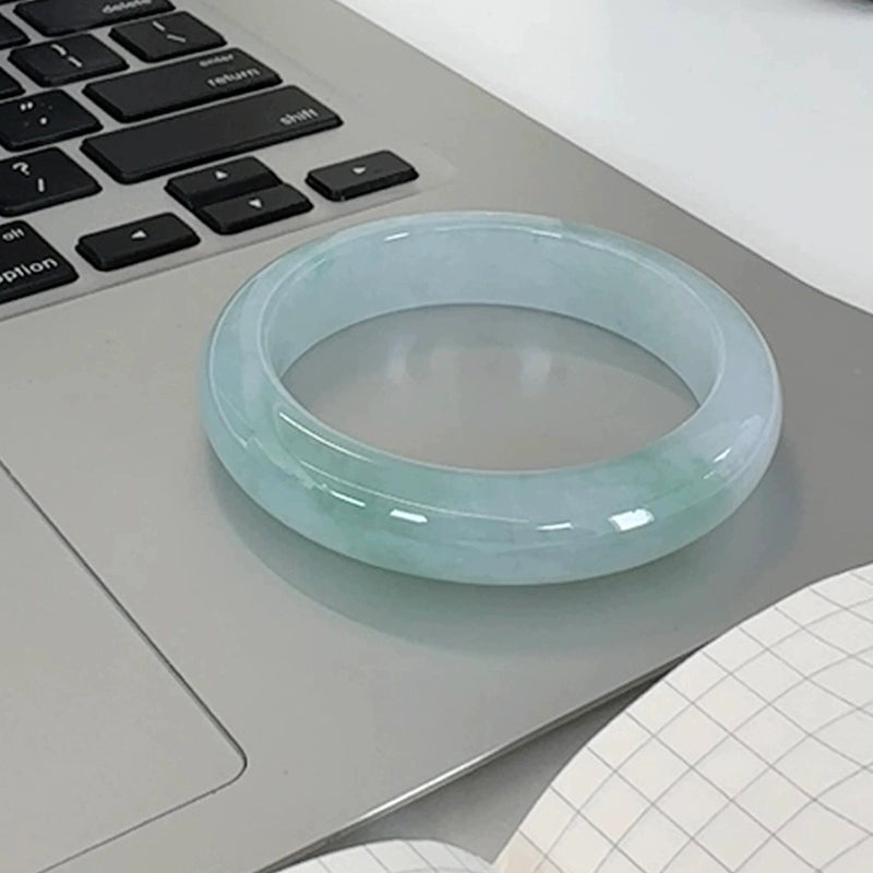 Hand holding natural light green gradient jadeite bangle with office desk background