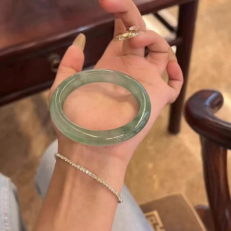 Hand holding natural light green icy jade bangle stacked with dainty chain