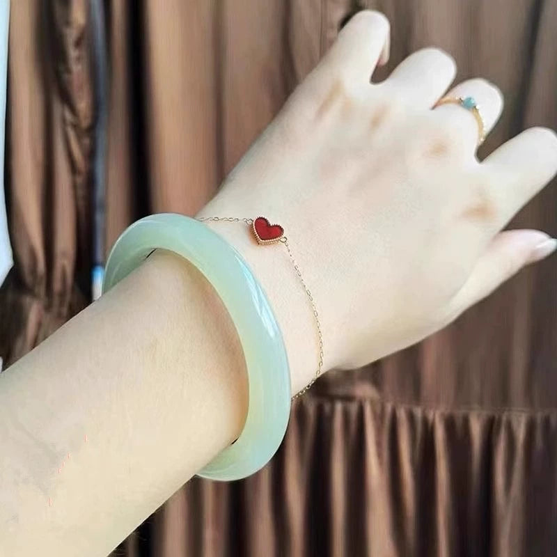 Hand wearing natural light green jade bangle and red heart charm bracelet