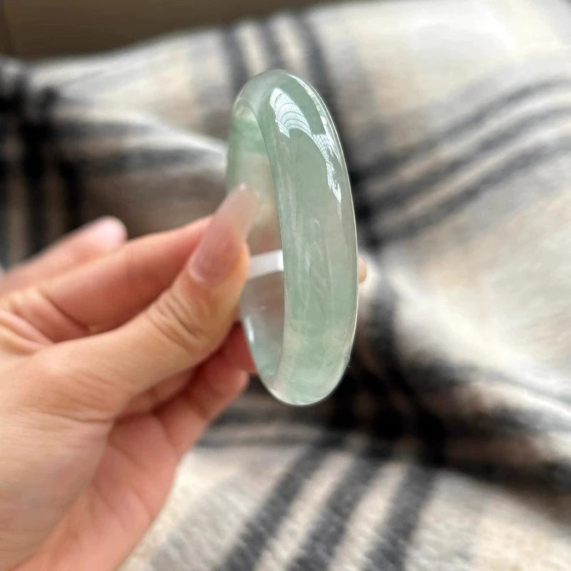 Hand holding natural light green jadeite bangle against plaid fabric background