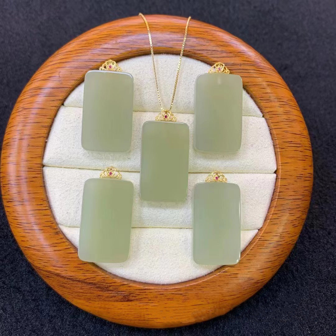 Set of natural nephrite jade bamboo - shaped pendants, each with gold - plated attachments, displayed on a round wooden jewelry tray with a soft, white - cushioned interior. One pendant is on a gold - toned chain, while the others are placed separately. 01