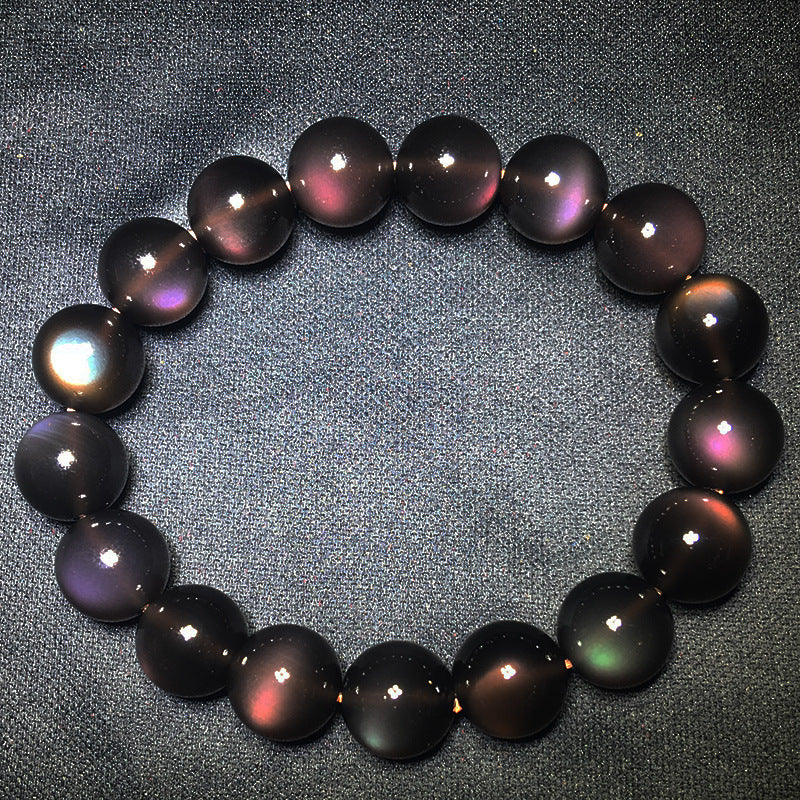 A natural rainbow obsidian bead bracelet with a distinct silver - sheen effect, placed on a wooden surface alongside a carved wooden box and a fallen autumn leaf