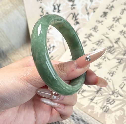 Hand holding natural rich green jade bangle with Chinese calligraphy background